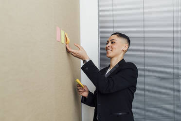 Female professional sticking adhesive notes on wall in office - MEUF02574