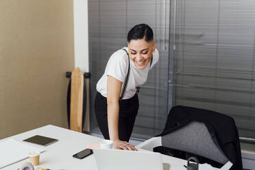 Smiling female entrepreneur looking at laptop during video call in office - MEUF02590