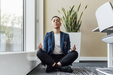 Young female entrepreneur meditating while sitting in office - MEUF02601