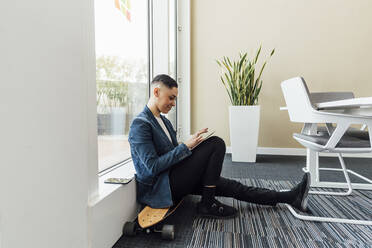 Entrepreneur using digital tablet while sitting on skateboard in office - MEUF02605
