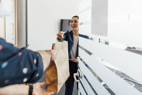 Smiling businesswoman taking food delivery in office - MEUF02609