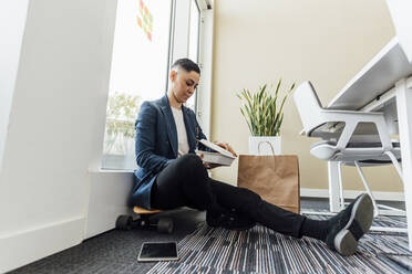 Female entrepreneur opening food box while sitting on skateboard in office - MEUF02611