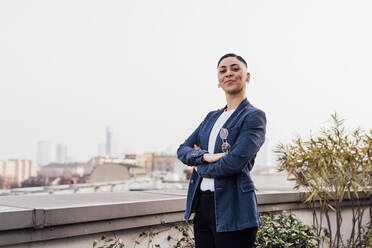 Young confident entrepreneur standing with arms crossed at rooftop - MEUF02616