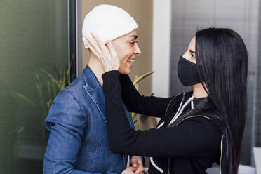 Eine Kollegin mit Gesichtsschutzmaske hilft einer Geschäftsfrau beim Anziehen im Büro - MEUF02618