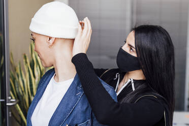 Eine Kollegin mit Gesichtsmaske hilft einer Geschäftsfrau mit Strickmütze im Büro - MEUF02619
