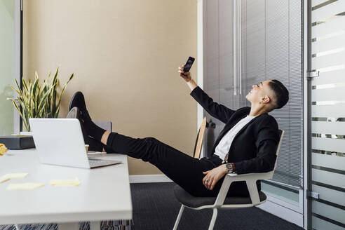 Lächelnde Geschäftsfrau nimmt Selfie durch Handy im Büro - MEUF02642