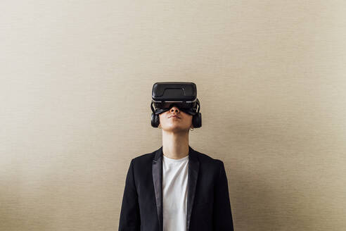 Geschäftsfrau mit Virtual-Reality-Headset vor einer Wand stehend - MEUF02647