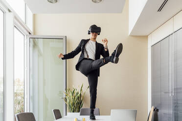 Junge Unternehmerin mit Virtual-Reality-Headset, die auf dem Schreibtisch im Büro steht und tritt - MEUF02657