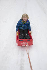 Fröhlicher Junge beim Rodeln auf Schnee im Winter - FVDF00009