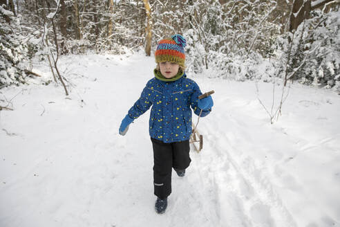 Niedlicher Junge, der im Winter einen Schlitten durch den Schnee zieht - FVDF00011