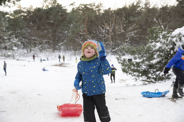 Playful boy with toboggan standing on snow - FVDF00013