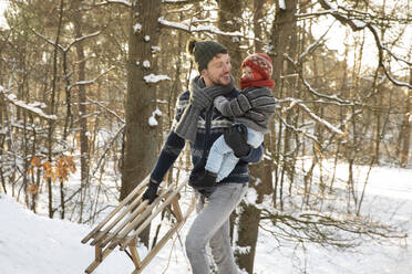 Vater mit Schlitten und Sohn beim Winterspaziergang im Schnee - FVDF00020