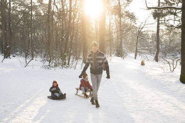 Vater zieht seine Söhne auf einem Schlitten im Schnee sitzend an einem sonnigen Tag - FVDF00024