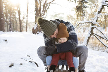 Vater umarmt seinen Sohn, während er im Winter auf dem Schlitten sitzt - FVDF00028