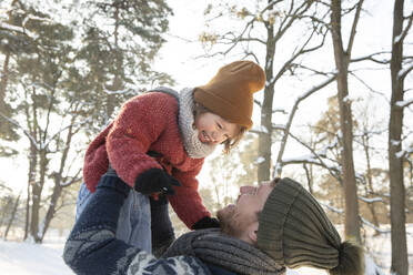 Cheerful father lifting son in warm clothing during winter - FVDF00034