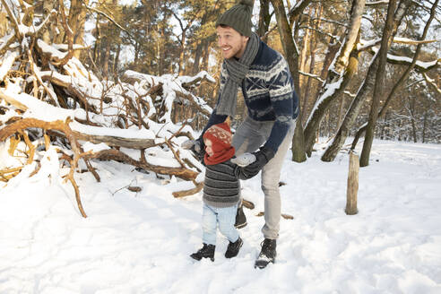 Vater hält sich an den Händen, während er im Winter mit seinem Sohn im Schnee spazieren geht - FVDF00036