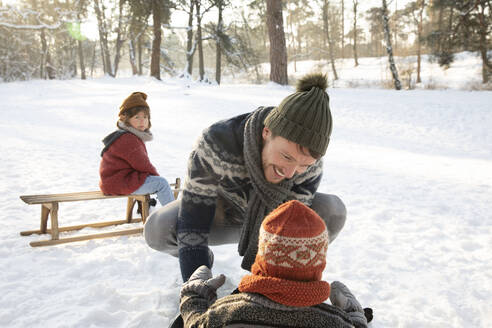 Lächelnder Vater in warmer Kleidung, der im Winter mit seinem Sohn im Schnee spielt - FVDF00038