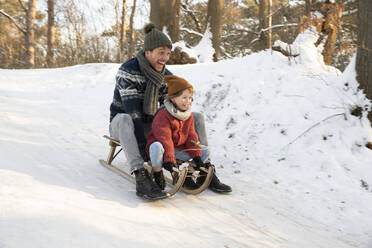 Verspielter Vater und Sohn beim Schlittenfahren auf Schnee im Winter - FVDF00040