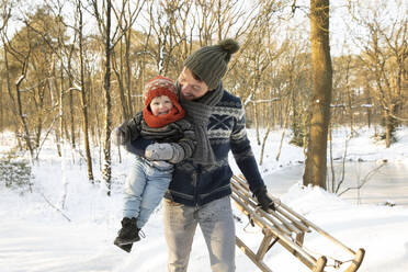 Glücklicher Vater, der seinen Sohn trägt, während er den Schlitten im Winter im Schnee hält - FVDF00046