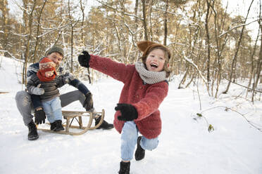 Playful boy on snow while father sitting with younger son on sled in background - FVDF00049