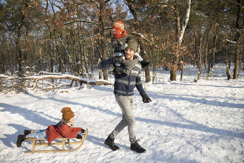 Vater trägt seinen Sohn auf der Schulter, während er im Winter einen Schlitten durch den Schnee zieht - FVDF00054
