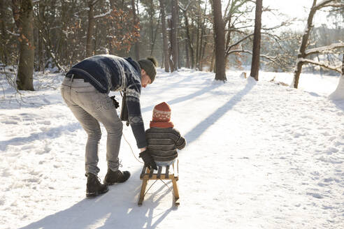 Father teaching sledding to son on snow during sunny day - FVDF00070