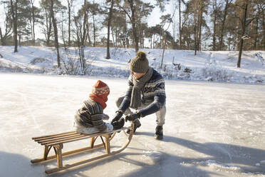 Father teaching sledding to son while crouching on snow during winter - FVDF00073