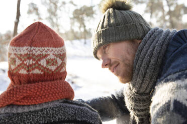 Vater mit Strickmütze sieht seinen Sohn im Winter an - FVDF00075