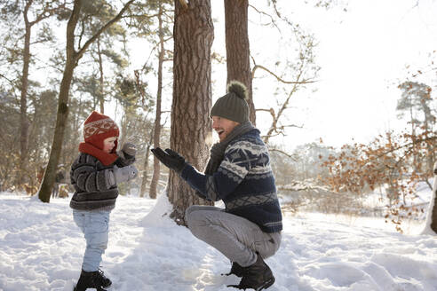 Vater spielt mit seinem Sohn, während er im Winter im Schnee hockt - FVDF00079