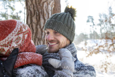 Lächelnder Vater mit Strickmütze sieht seinen Sohn im Winter an - FVDF00084