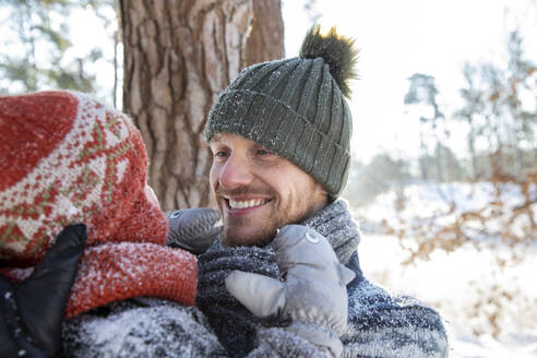 Lächelnder Vater mit Strickmütze sieht seinen Sohn im Winter an - FVDF00084