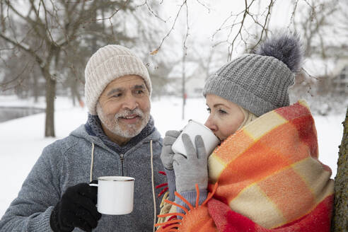 Mann sieht Frau an, die im Winter Tee in einem Becher trinkt - FVDF00095