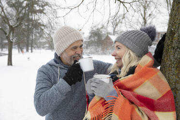 Lächelndes älteres Paar, das im Winter Tee in einer Tasse trinkt - FVDF00096