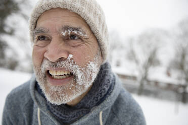 Smiling man looking away with snow on face during winter - FVDF00107