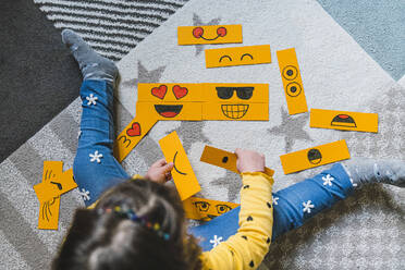 Mädchen spielt mit gelbem Papier Emoticons, während auf Teppich zu Hause sitzen - MGIF01101