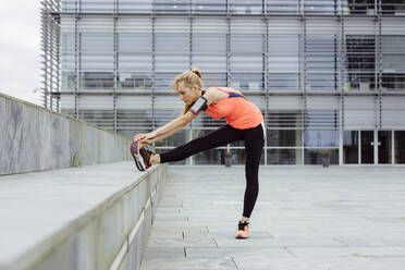 Side view of pretty blonde young woman stretching on the street before running - ADSF23552