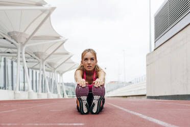 Hübsche blonde junge Frau in Sportkleidung, die auf dem Boden sitzt und sich dehnt, bevor sie wegläuft und wegschaut - ADSF23557