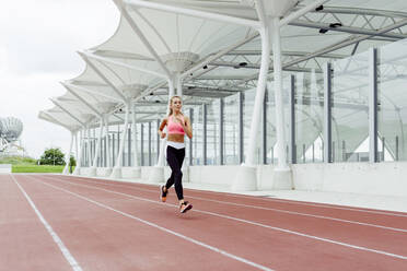 Attraktive junge Sportlerin in Sportkleidung beim Laufen auf dem Sportplatz - ADSF23561