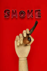 Top view of pipe in wooden hand placed on red background with Smoke word made of metal letters - ADSF23590