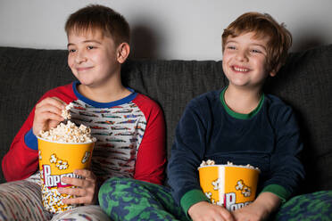 Junge kleine Brüder sitzen gemütlich auf dem Sofa mit Popcorn-Eimer beim Essen und Fernsehen - ADSF23623