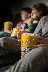 Cropped junge erstaunt Geschwister Kinder sitzen bequem auf Sofa mit Popcorn-Eimer beim Essen und Fernsehen - ADSF23624