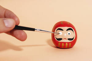 Hand einer Person, die Details einer traditionellen japanischen Daruma-Puppe malt - GEMF04759