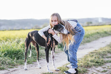 Blond girl embracing dog on footpath - JCMF01946