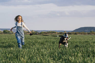 Smiling playful girl running dog on agricultural field - JCMF01949