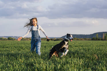 Aufgeregtes Mädchen mit Hund läuft über Feld - JCMF01950