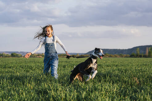 Excited girl with dog running over field - JCMF01950