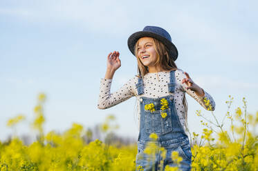 Cheerful girl wearing sun hat standing at agricultural field - JCMF01958