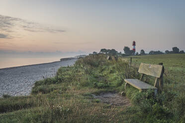 Deutschland, Schleswig-Holstein, Pommerby, Leere Strandbank in der Abenddämmerung mit Leuchtturm Falshoft im Hintergrund - KEBF01862