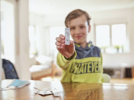 Lächelnder Junge zeigt eine Probe des diagnostischen Schnelltests zu Hause - DIKF00570