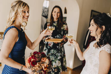 Glückliche Braut mit Freundinnen trinken Wein im häuslichen Raum - DAWF01961